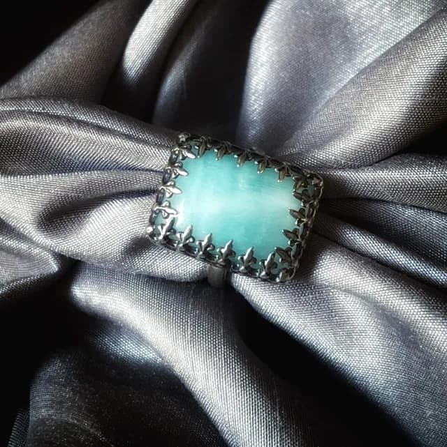 Vue plongeante de la bague artisanale avec pierre bleue claire et serti dentelé sur soie grise