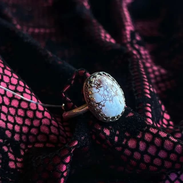 Bague avec cabochon ovale blanc veiné dans un serti argenté à griffes, sur tissu noir et rose.
