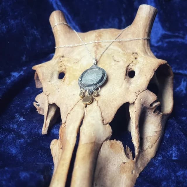 Collier talisman avec chaîne argentée et pendentif œil disposé sur un crâne décoratif.