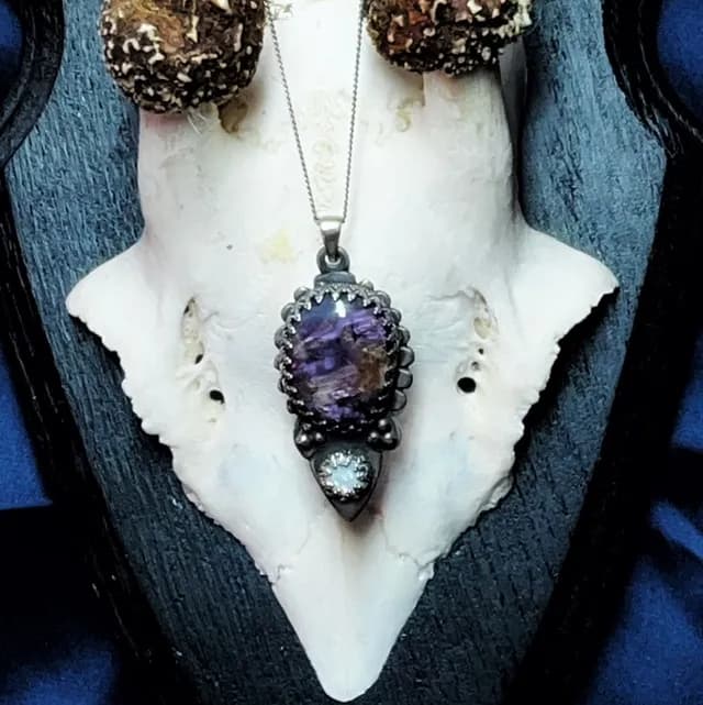 Gros plan sur le pendentif Éclipse serti d'une charoite violette et d'une opale