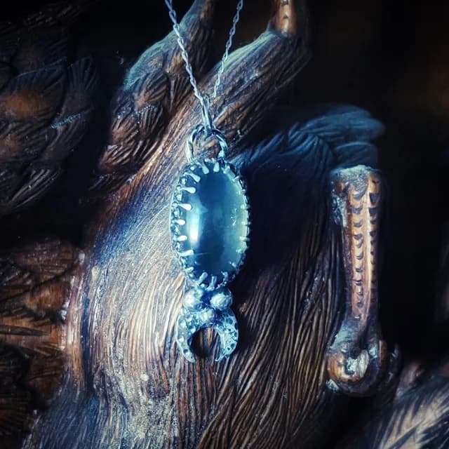 Vue rapprochée en biais du pendentif artisanal en argent avec cabochon gris et croissant lunaire.
