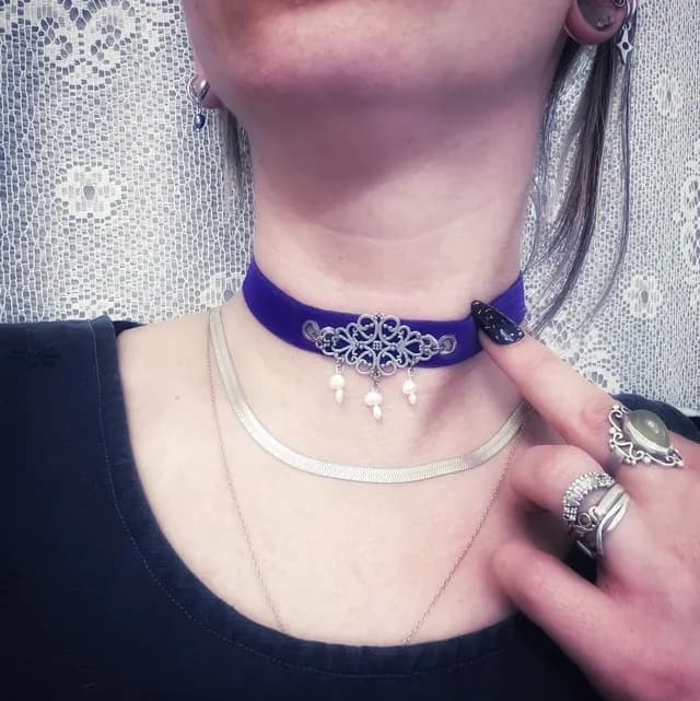 Collier ras de cou en velours violet avec motif métallique ajouré et perles pendantes porté au cou.