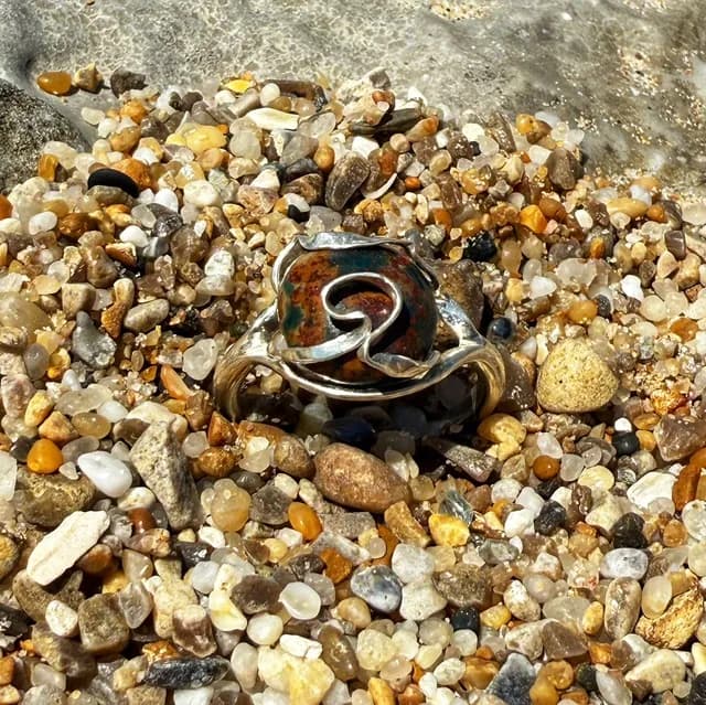 Vue de face de la bague en argent avec ruban ondulé retenant la pierre de jaspe océan sur des galets