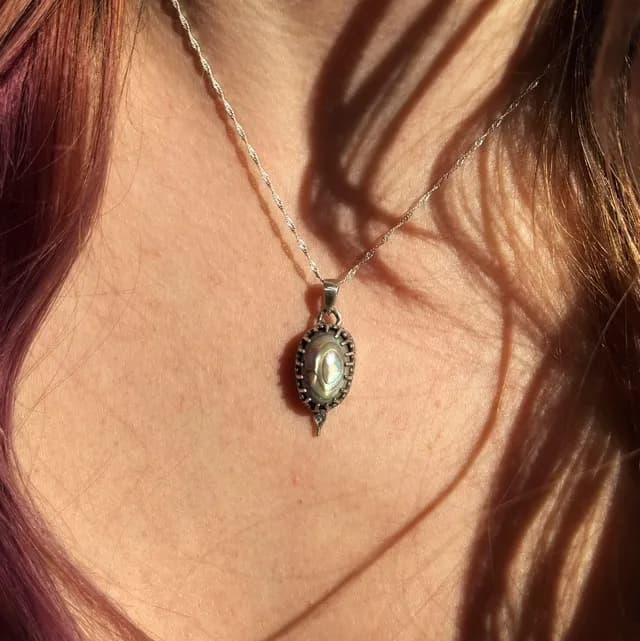 Pendentif en argent serti d'un cabochon en nacre abalone, porté au cou sur une fine chaîne torsadée.