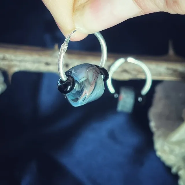 Gros plan sur une créole tenue en main ornée d'une perle en verre filé marbrée et de deux perles noires.