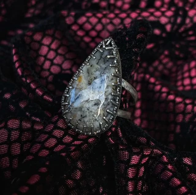 Bague en argent avec pierre taillée en goutte posée sur une dentelle rose et noire.