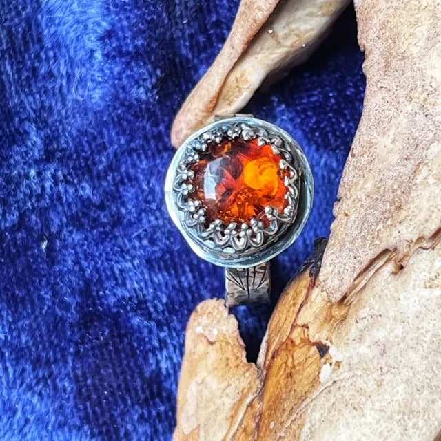 Gros plan sur le cabochon d'ambre cognac serti dans une bordure en argent dentelée façon couronne.