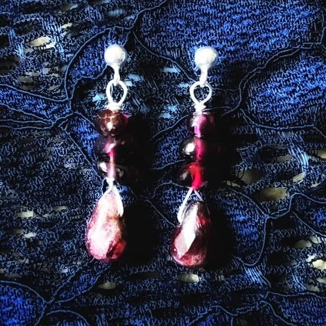 Détail de boucles d'oreilles pendantes artisanales montées sur fil d'argent.