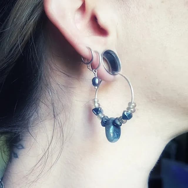Créole Notte portée à l'oreille, garnie de perles foncées et d'un pendentif en agate naturelle.