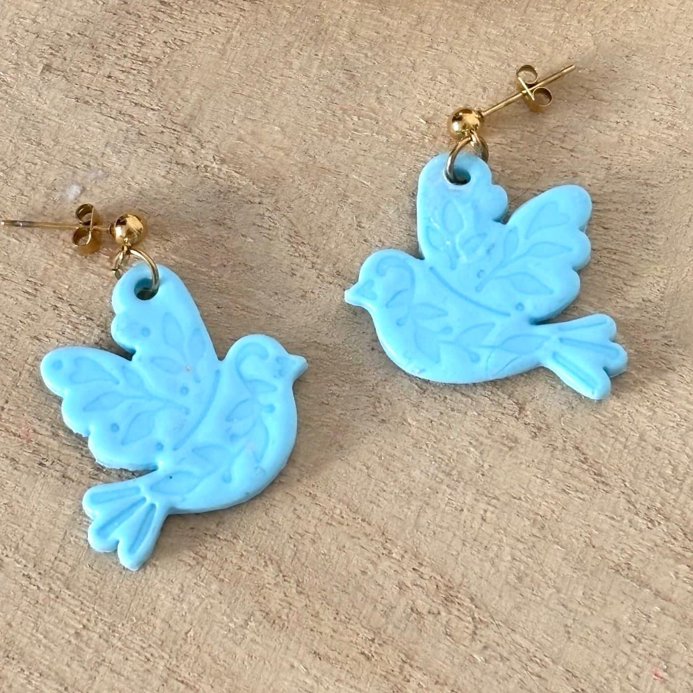 Boucles d'oreilles oiseau bleu clair ornées de motifs végétaux sur fond en bois
