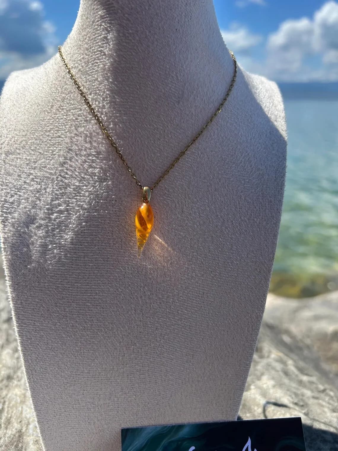 Boucles d'oreilles orange et pendentif assorti présentés au bord de l'eau.