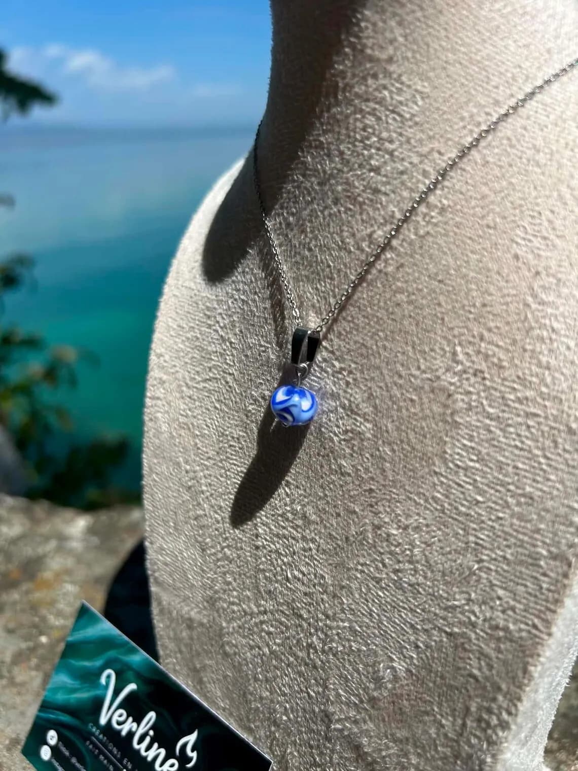 Pendentif en verre filé bleu et blanc monté sur chaîne en acier inoxydable sur buste.