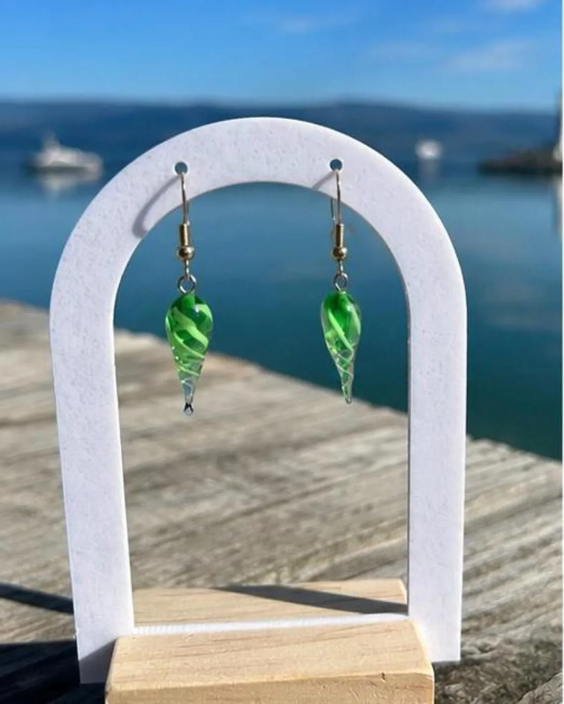 Paire de boucles d'oreilles pendantes vertes et blanches sur présentoir face à la mer