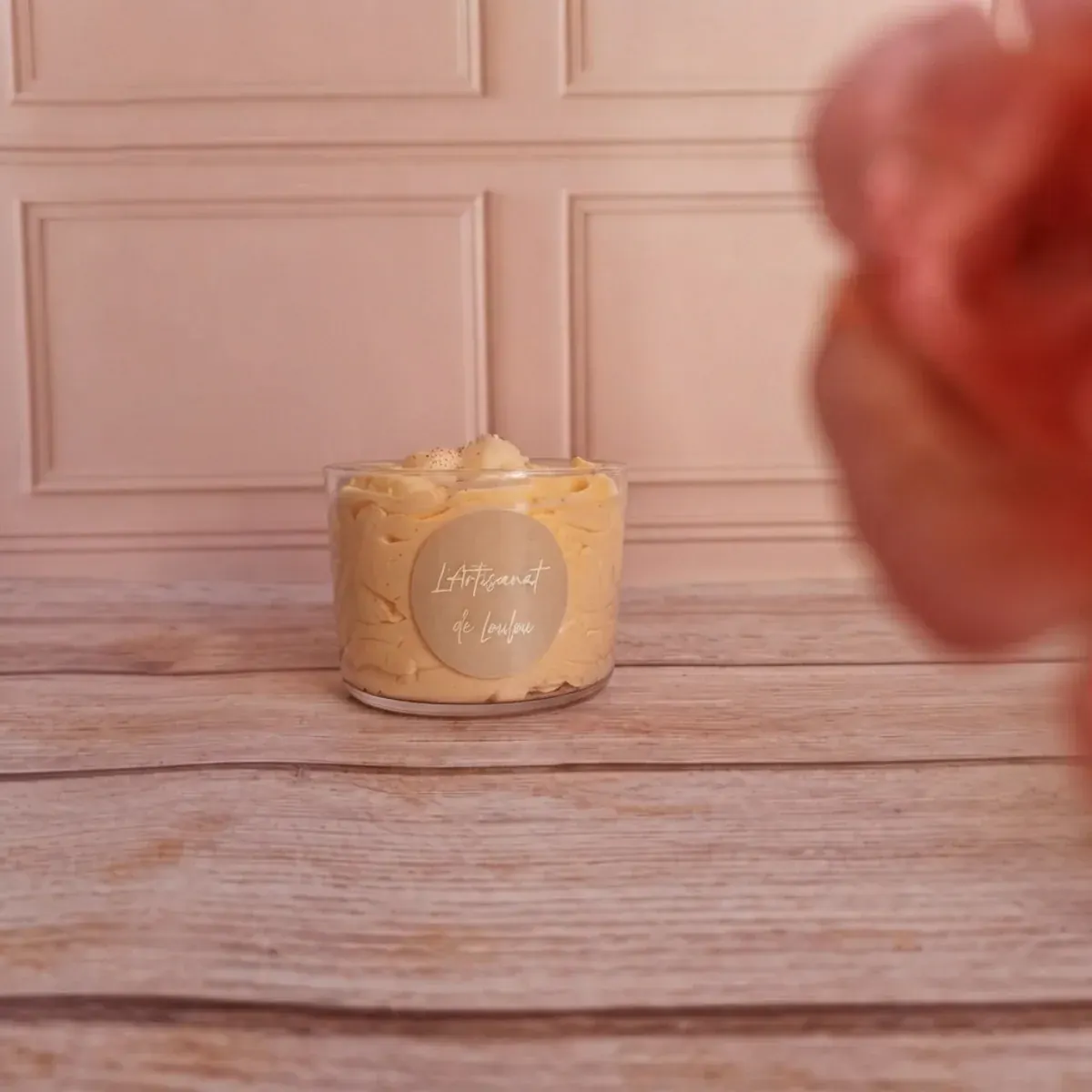 Bougie parfumée en pot transparent avec étiquette ronde, posée sur une table en bois clair.