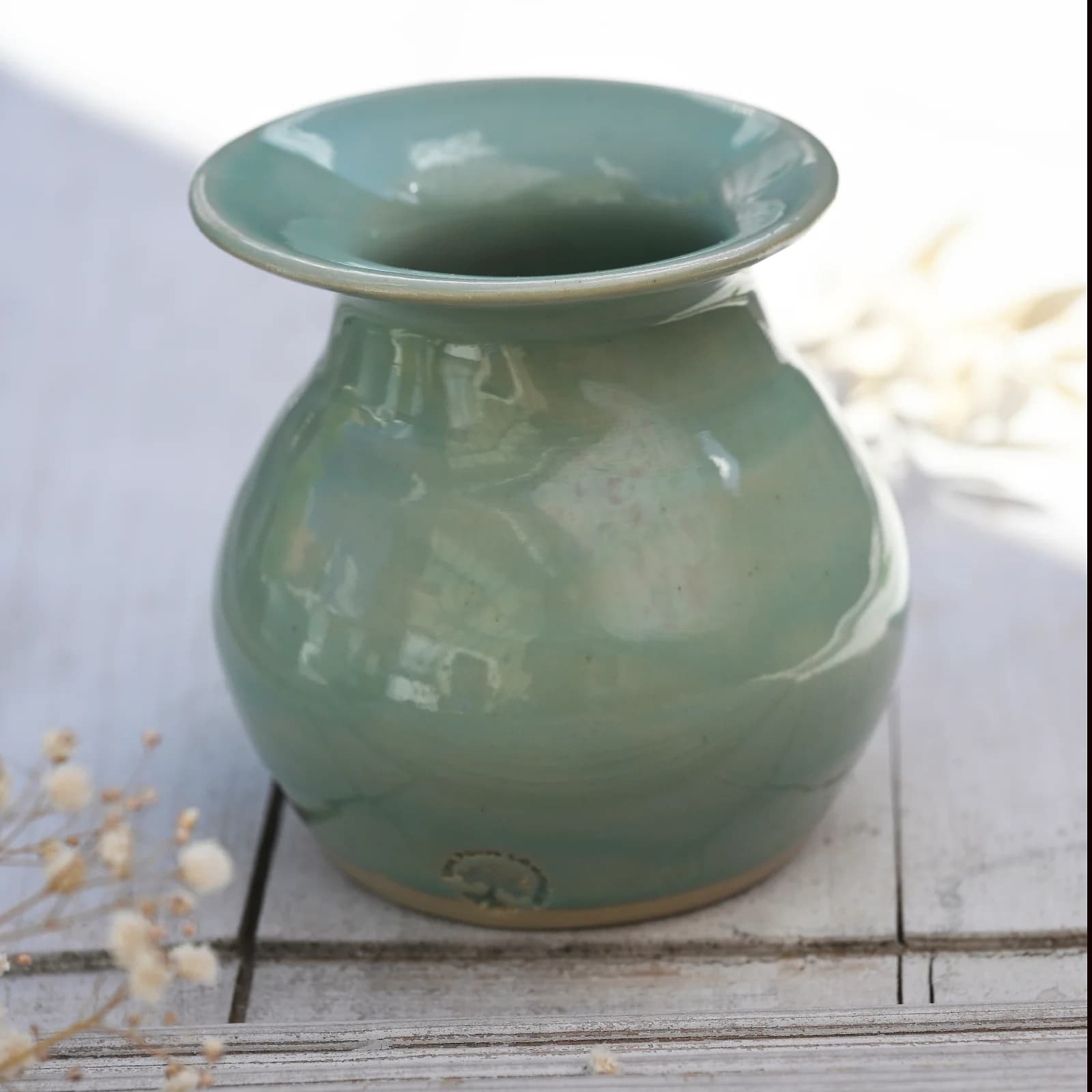 Vase galbé en céramique émaillée vert céladon avec col ouvert, posé sur une surface en bois clair.