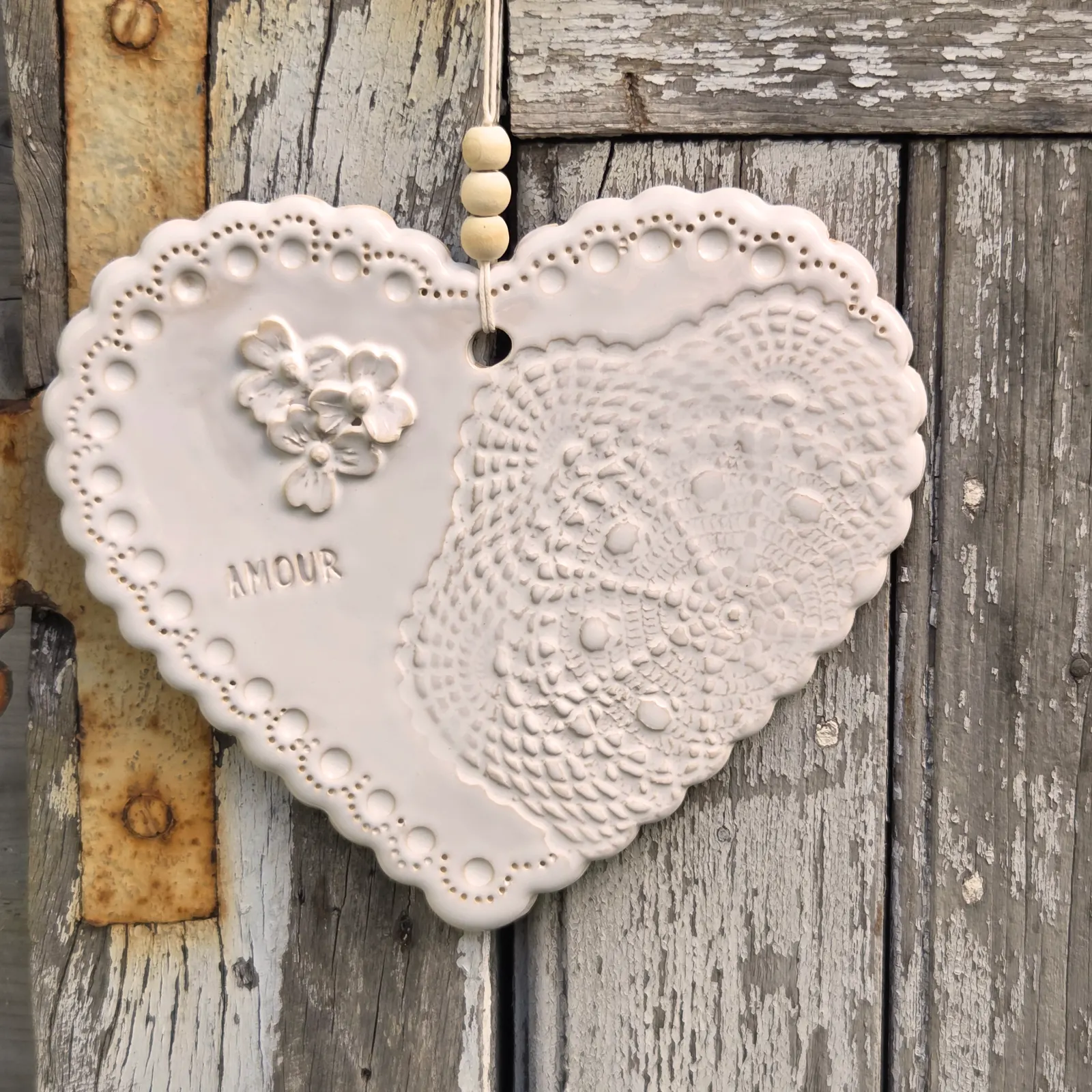 Suspension cœur en céramique blanche ornée d'un motif dentelle, d'un bouquet de fleurs et du mot Amour