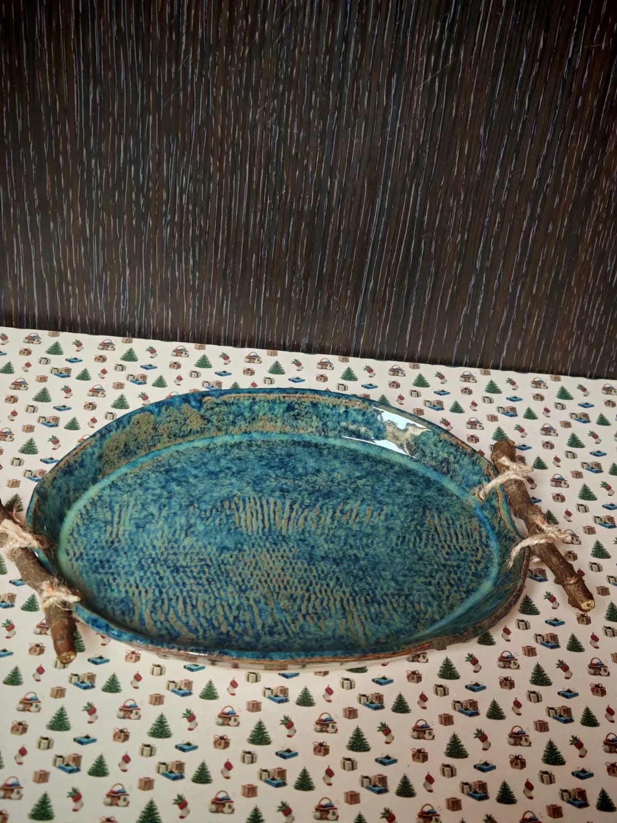 Plat ovale artisanal en céramique émaillée bleue texturée avec poignées en bois.