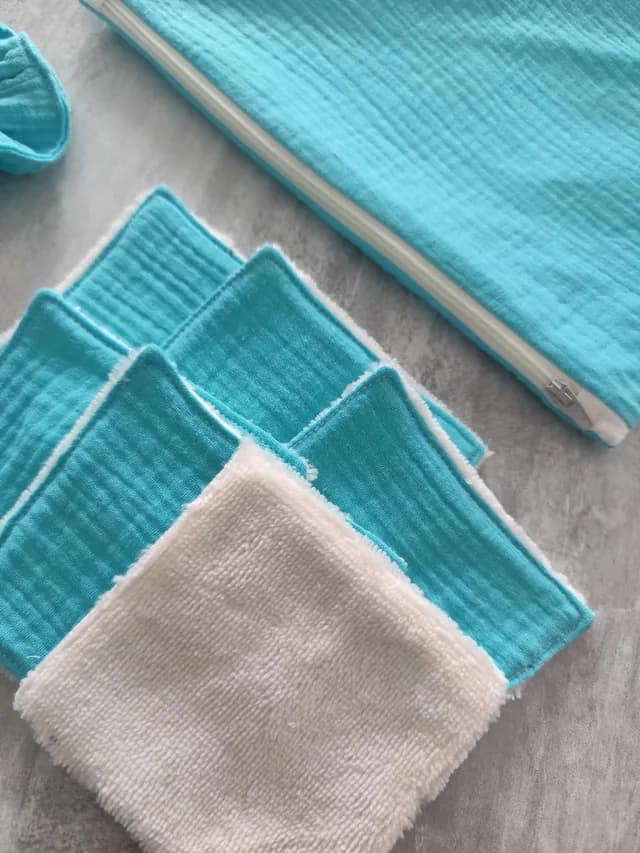 Gros plan sur les lingettes lavables turquoise et blanches à côté de la pochette zippée.
